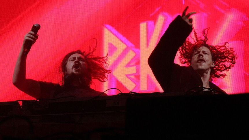 Two men in a band on stage at a music festival.