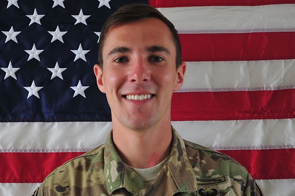 Dillon Baldridge poses in his military uniform in front of a US flag.