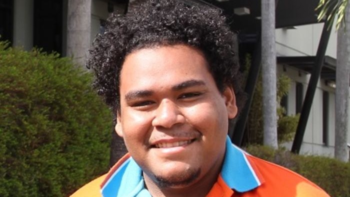 A young man with a big smile in an orange polo shirt.