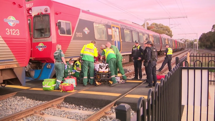 Paramedics and police officers treat a man on a stretcher next to a train on the tracks