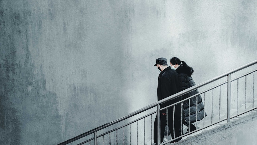 A man and woman walk down the stairs - both are wearing masks