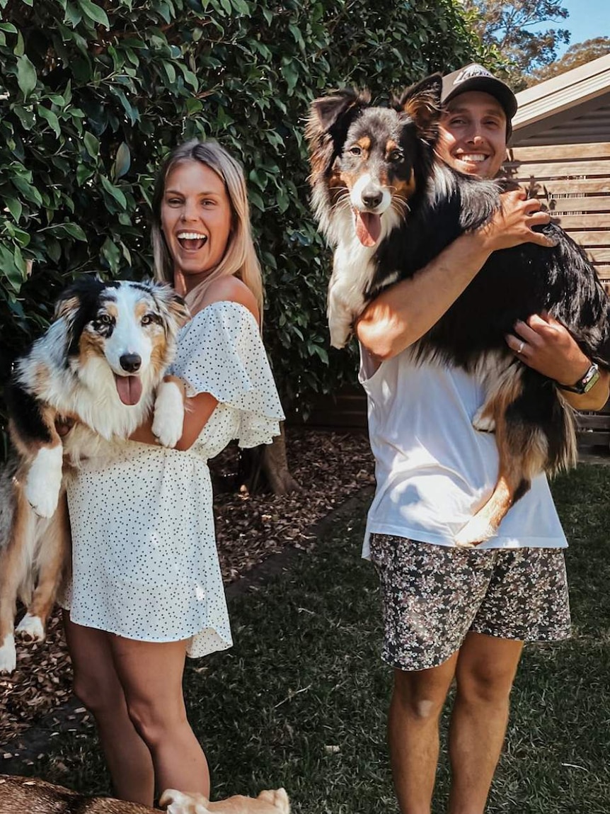 Jess and her husband smile at the camera holding their two sheep dogs