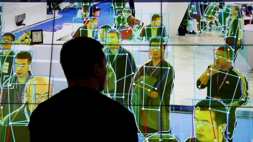 A man looks at a demonstration on a big screen of software tracking the movement of people.