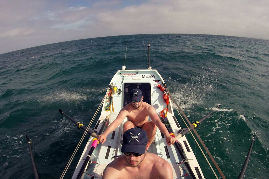 Two shirtless men rowing a boat on the ocean