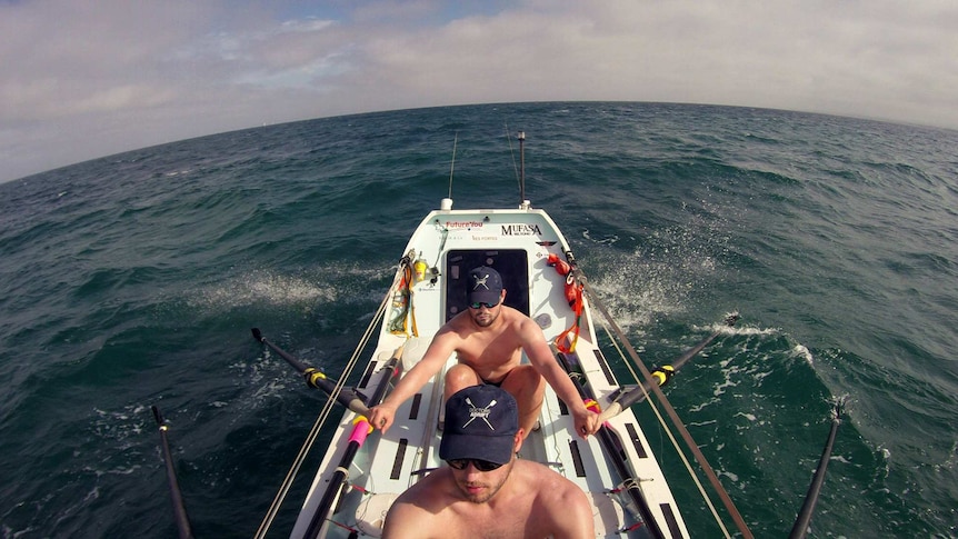 Two shirtless men rowing a boat on the ocean