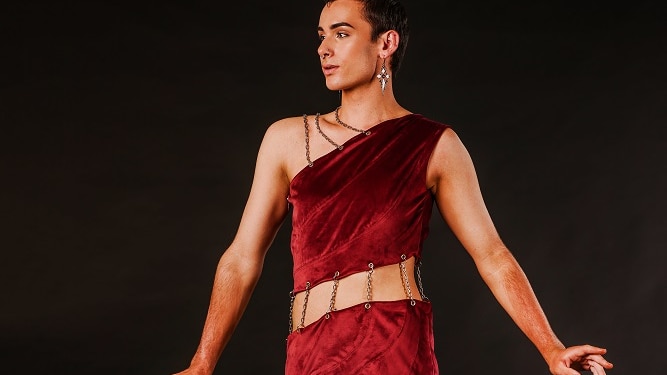A young man wearing a form fitting red dress cut in three sections held together by metal links.