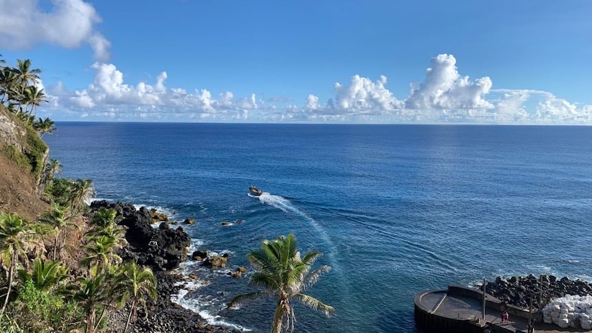 Sunny day with deep blue water, showing a boat pulling away from Pitcairn Islands. 
