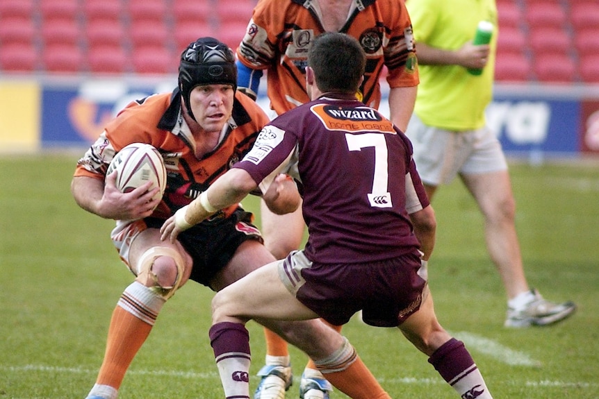 A football player in orange runs towards his opposition in maroon