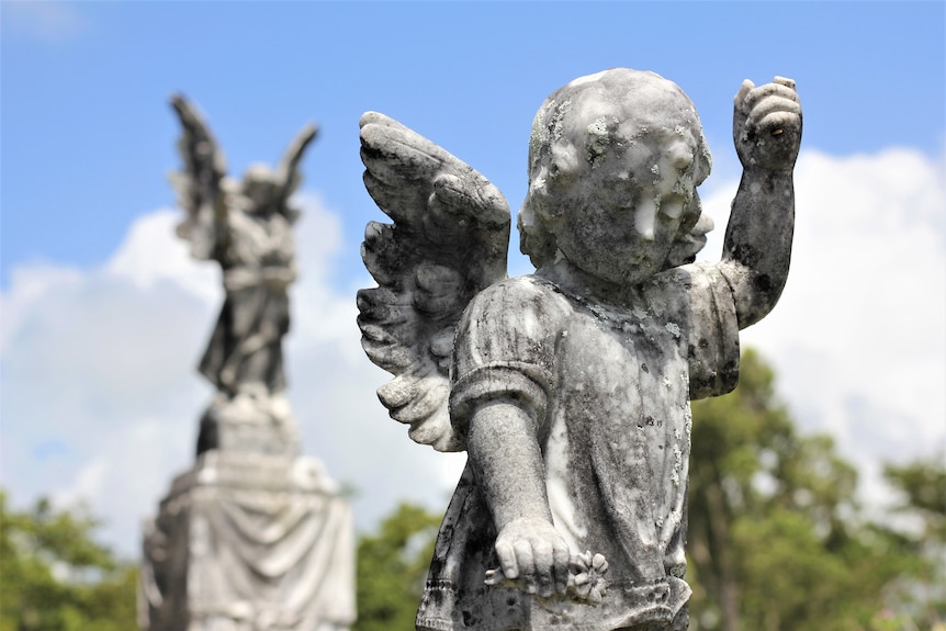 A marble statue of a winged angel with its hand in the air.