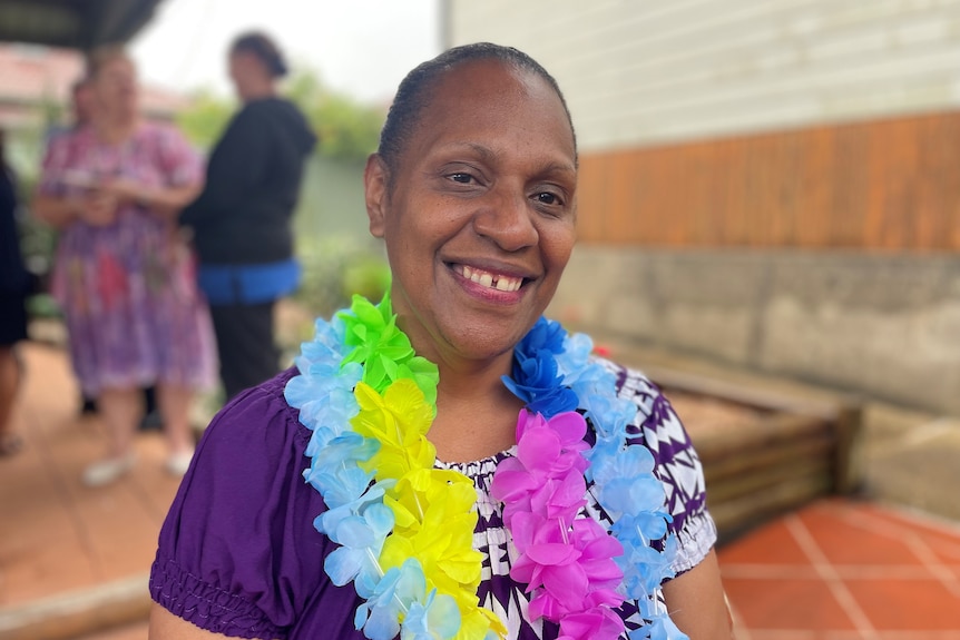 A woman from Vanuatu smiling, wearing a bright purple dress and flowers around her neck.