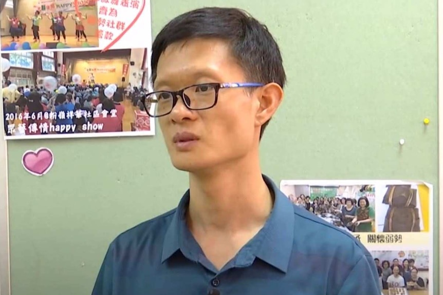 A man stands in front of green walls with posters stuck to them.