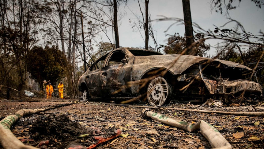 Emergency crews survey the scene after a bushfire, beyond a burnt out car