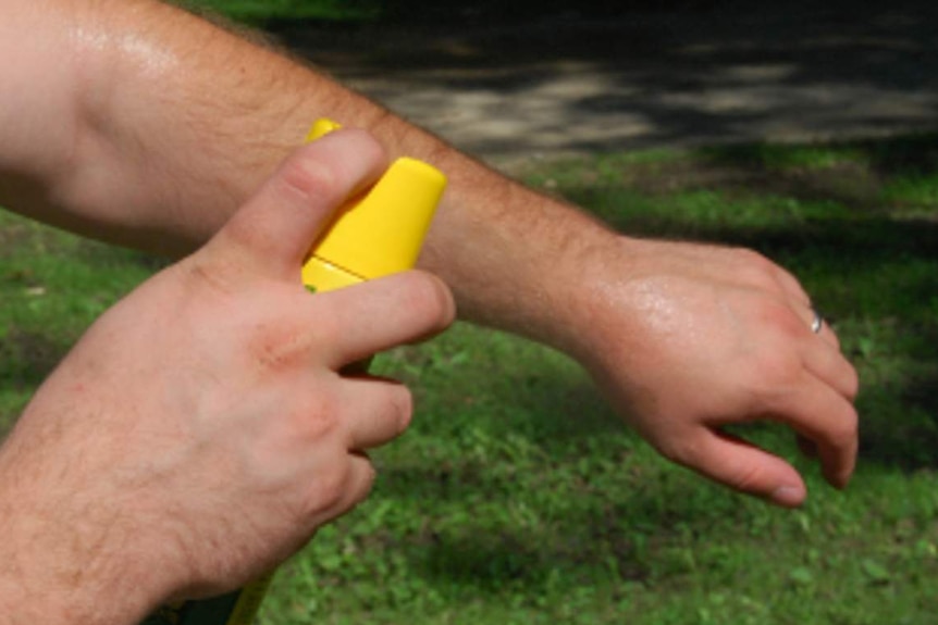 Un hombre se rocía el brazo con repelente.