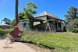 A wooden red and white colored Santa sits against a pole on the ground in front of a flood ravaged home. Santa is covered in mud