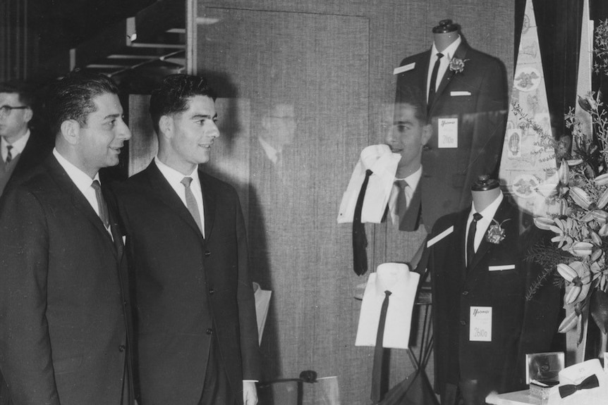 Two men in suits look in the window of a clothing store and menswear, black and white photo.