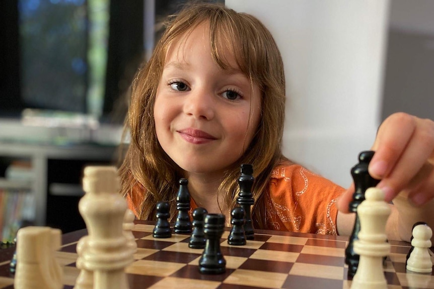 A girl in an orange t-shirt playing chess.