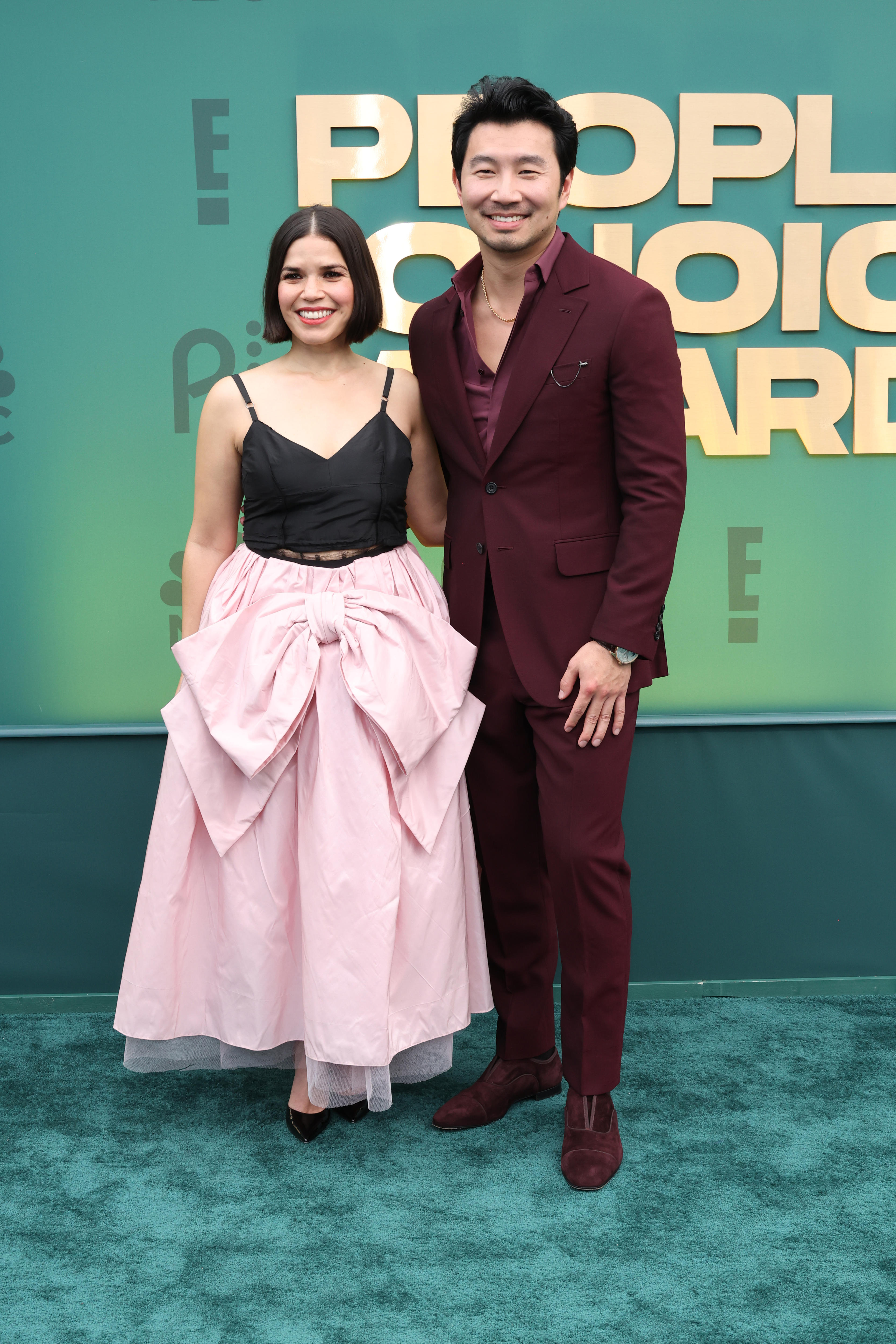 An actress in a black and pink gown standing next to an actor in a maroon suit on the red carpet