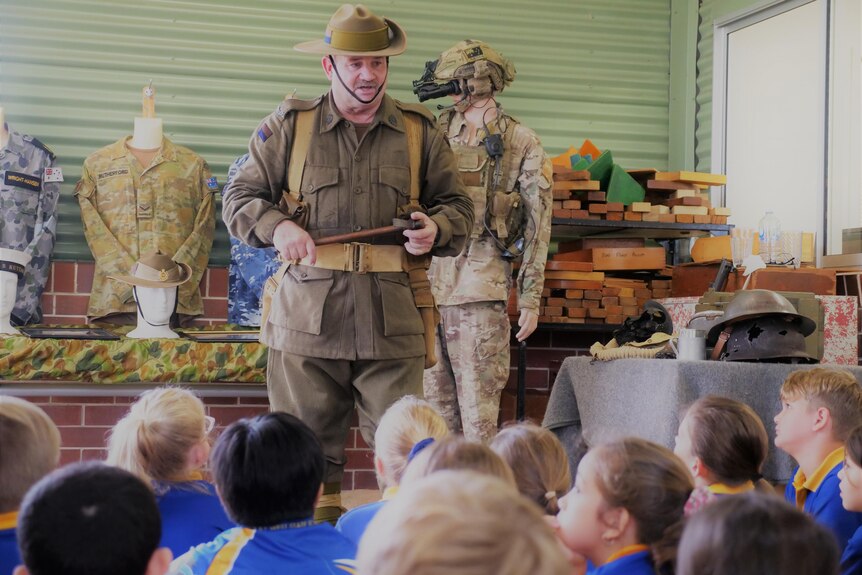 rows of students look up at a man dressed in a soldier's outfit as he gives a lesson