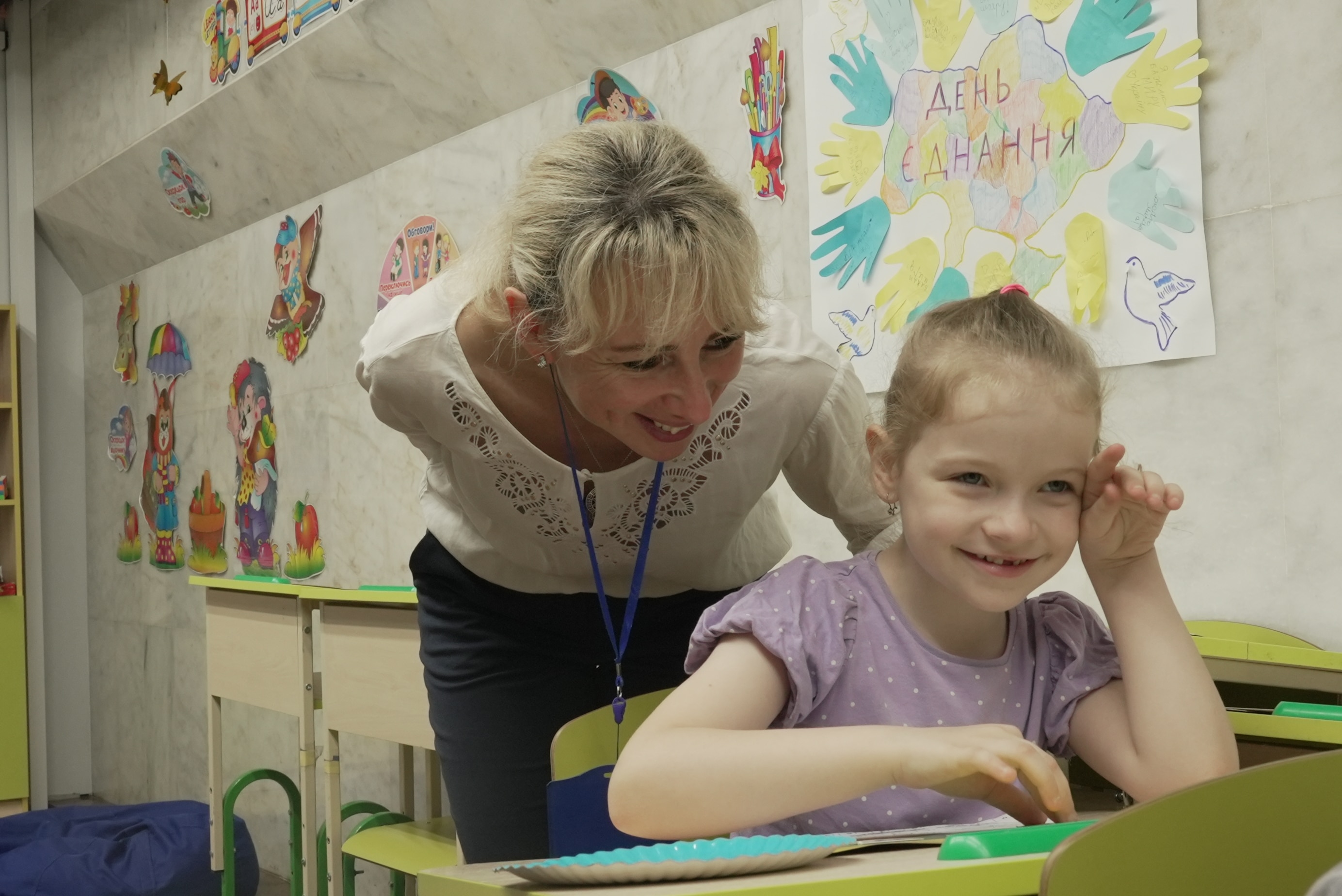 A little girl smiling with a woman leaning over behind her