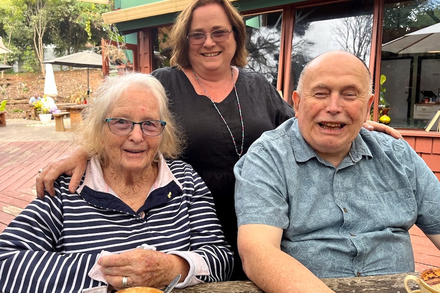 A woman stands behind two an older man and woman - all smiling