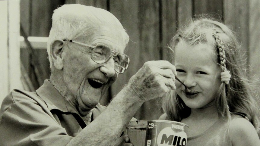 Black and white image of inventor Thomas Mayne smiling as he spoons dry Milo into an unknown child's mouth