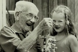 Black and white image of inventor Thomas Mayne smiling as he spoons dry Milo into an unknown child's mouth