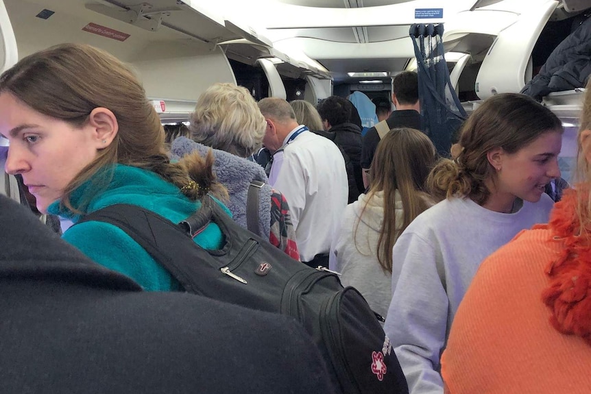 Passengers stand close together in the aisle of a plane.