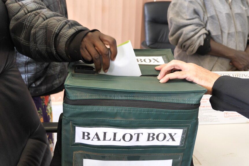 Someone's hand placing a voting slip into a ballot box