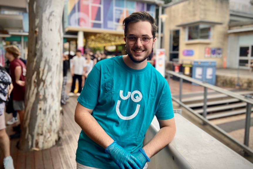 man in blue t-shirt smiling with food being served to a queue behind him