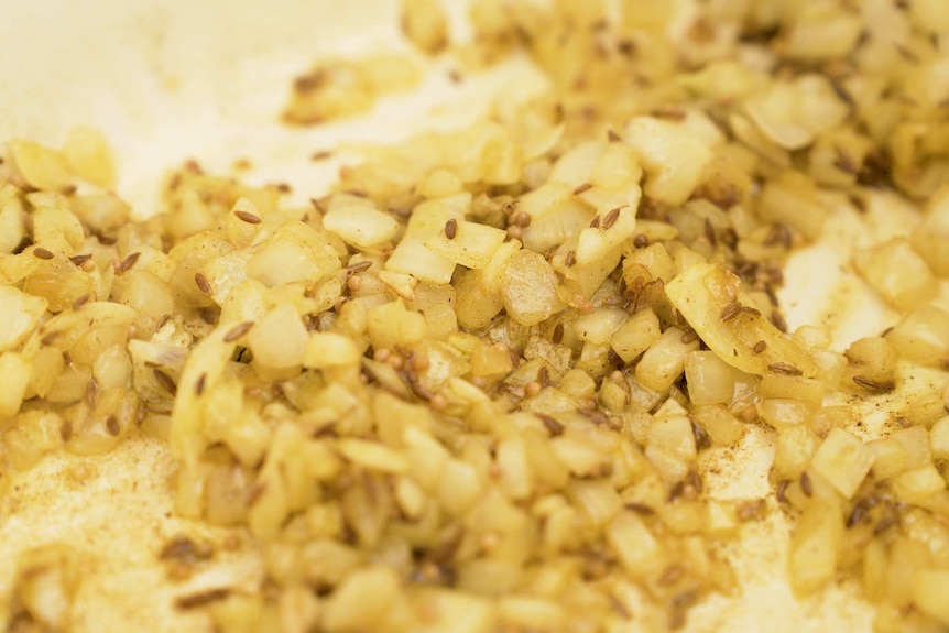 Onions being browned with ghee in a pan, along with spices to depict how to use ghee in cooking.