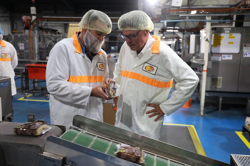 Two men wearing lab coats looking at a a packet of brown rice in a processin