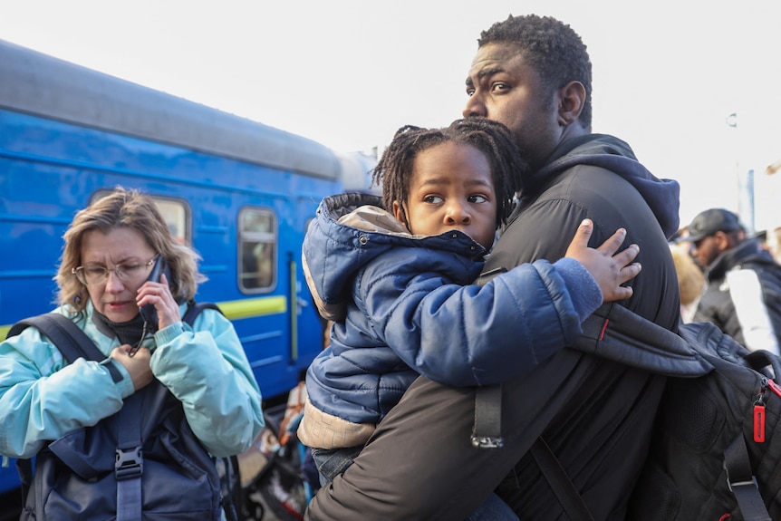 A father holds his young child outside a train.