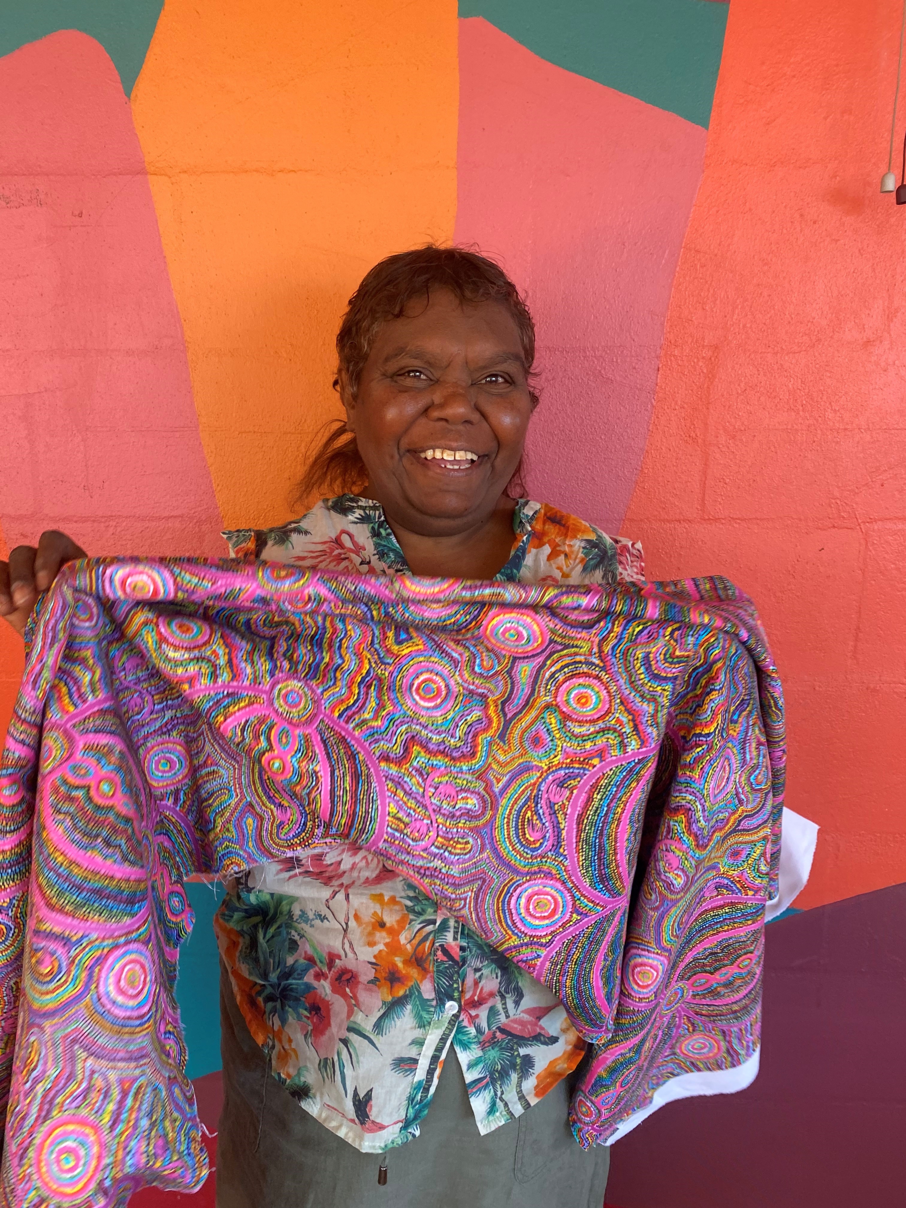 A woman holds up brightly coloured fabric by Indigenous artists.