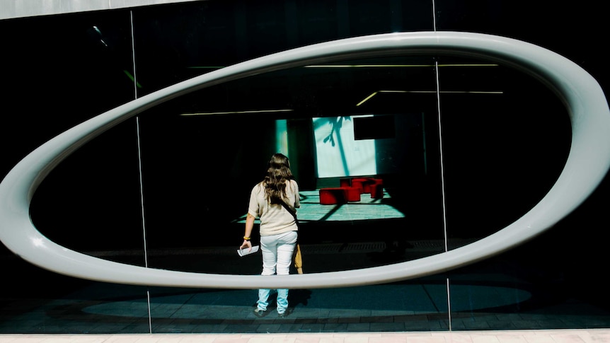 A woman stands in a window, framed by an oval sculptural feature.