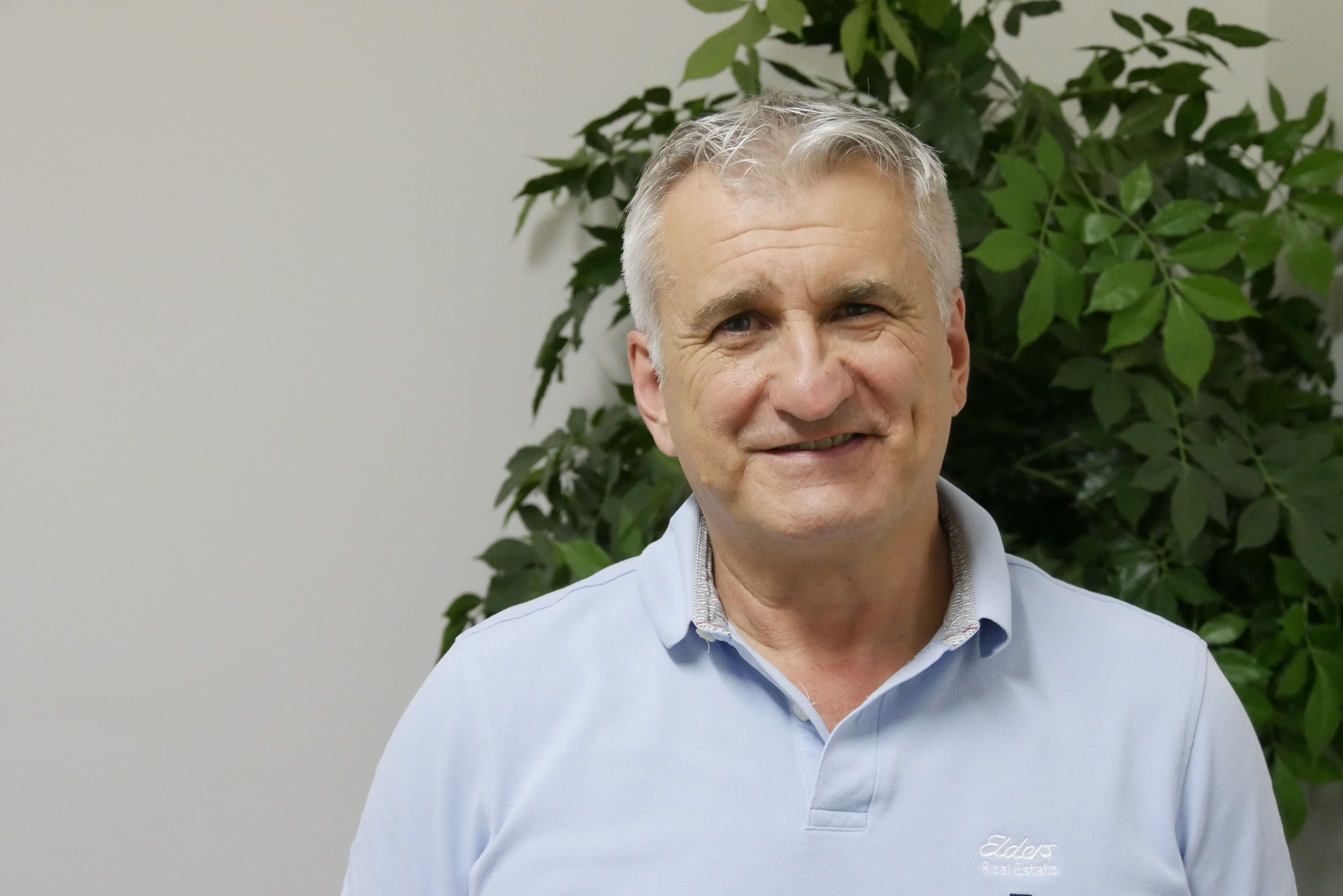Un hombre con un polo azul sonríe frente a una planta verde