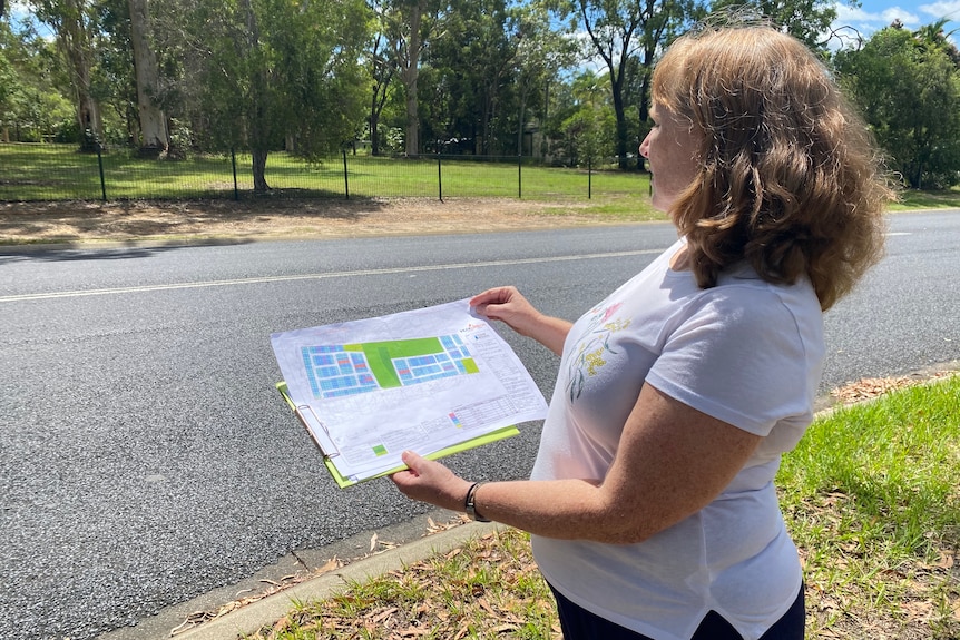Leah Campbell stands holding a map across the road from a proposed development.