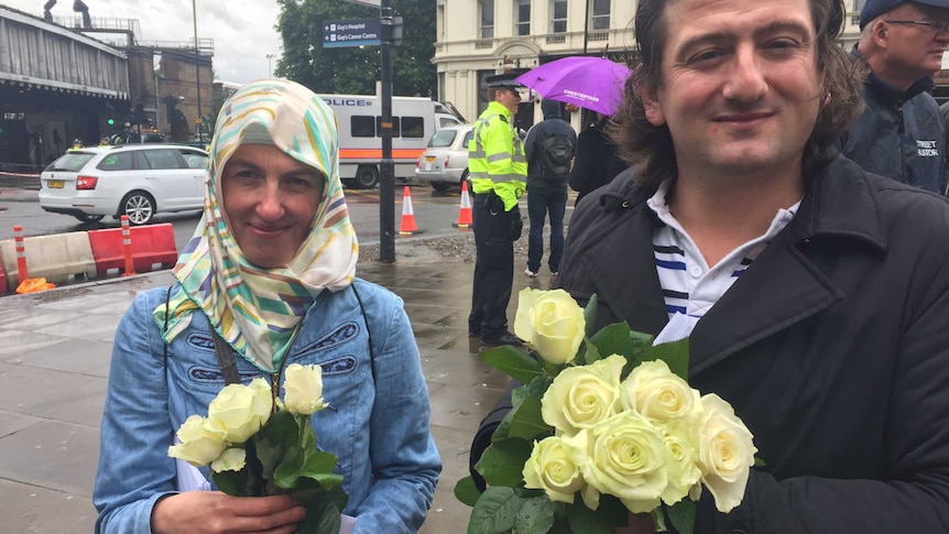 Beyza Coskun and Mutlu Sancaktutar stand side by side on a rainy day holding flowers.