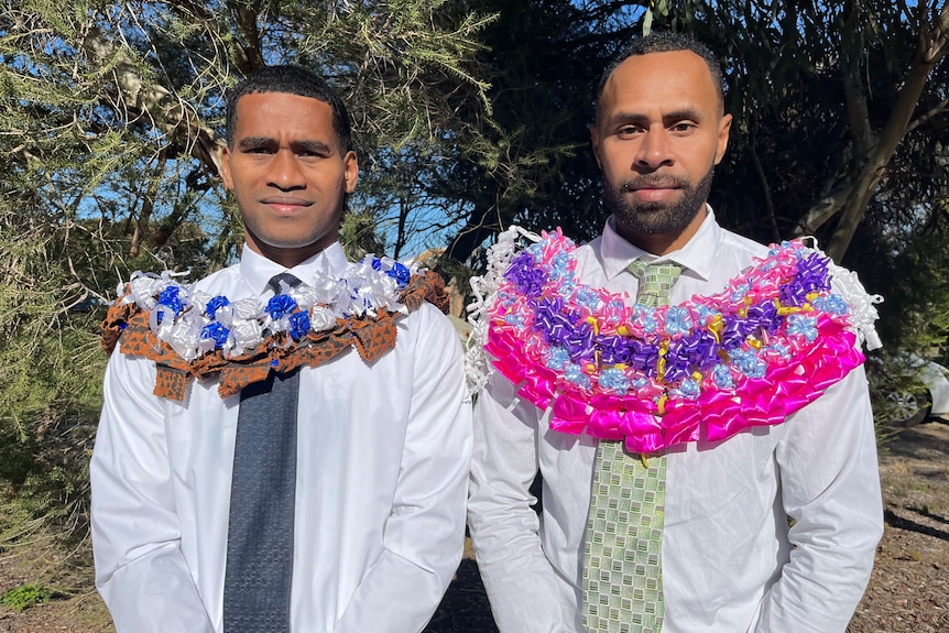 Two Fijian men wearing suits and a colourful wreath around their necks.