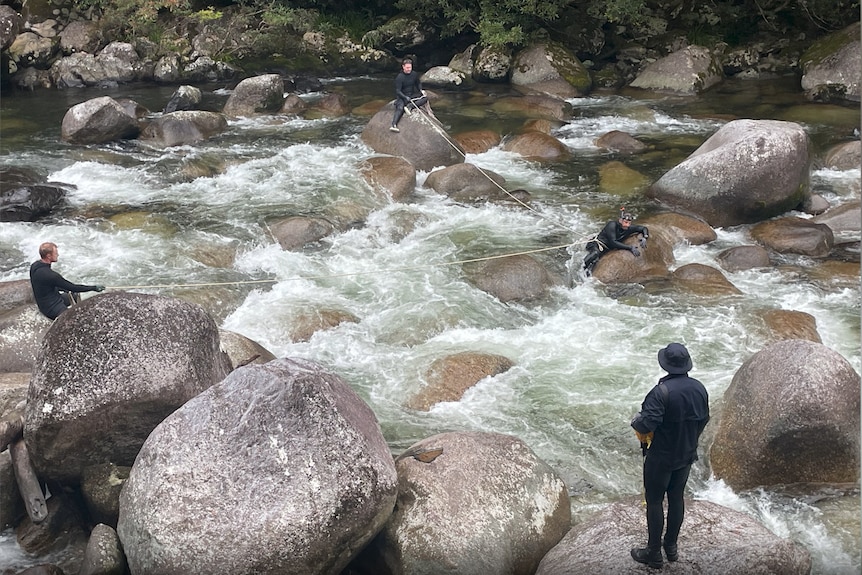 police standing in between rocks with fast rushing water around them