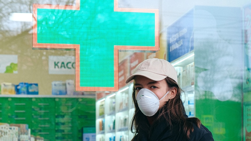 A woman wearing a mask outside a pharmacy