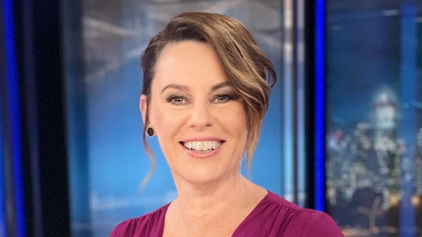 Mary Gearin sits behind a newsreading desk in the ABC studios with a keyboard and mouse, smiling at the camera.