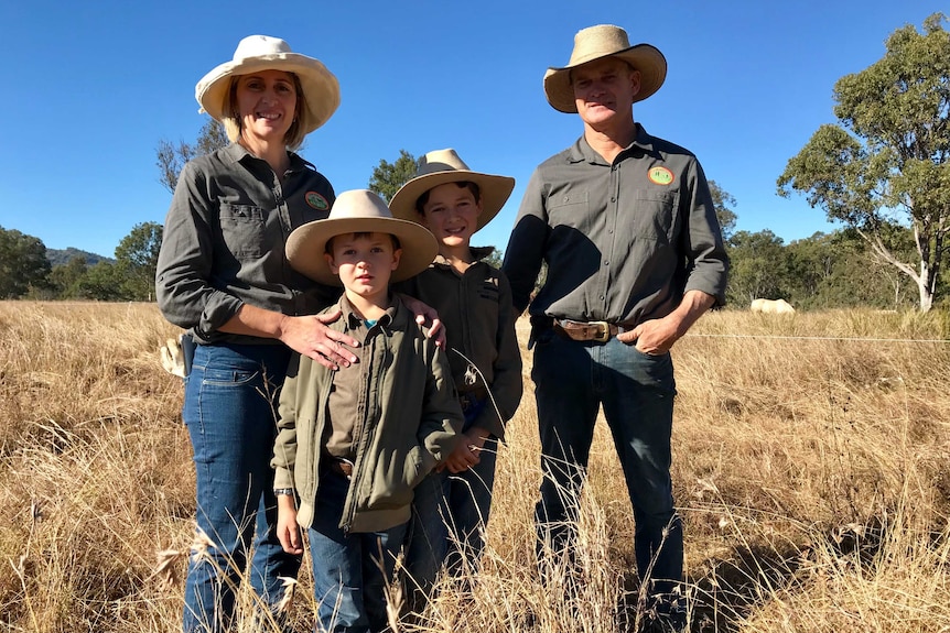 A family wearing hats under a hot blue sky, standing in long grass on their beef property.