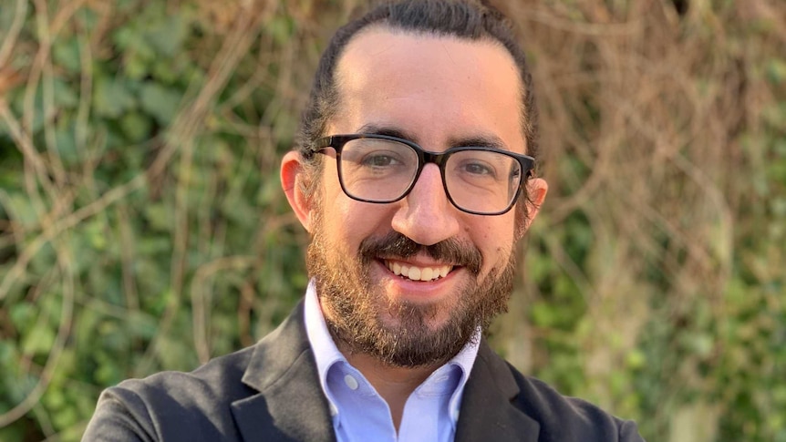 man with beard and glasses smiling at camera with arms crossed