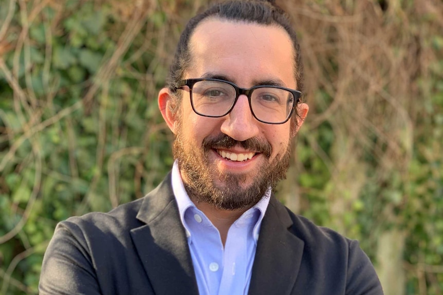 man with beard and glasses smiling at camera with arms crossed