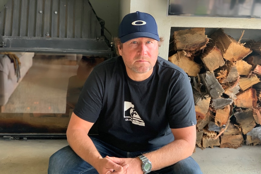 Man sits on a concrete step with a pile of firewood behind him