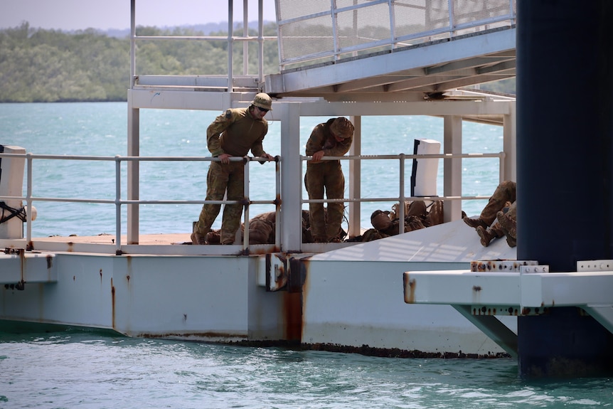 Military personnel are wearing cargo gear and standing on a ferry terminal. They are looking serious.