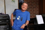 Children's entertainer Peter Combe leans against a piano.