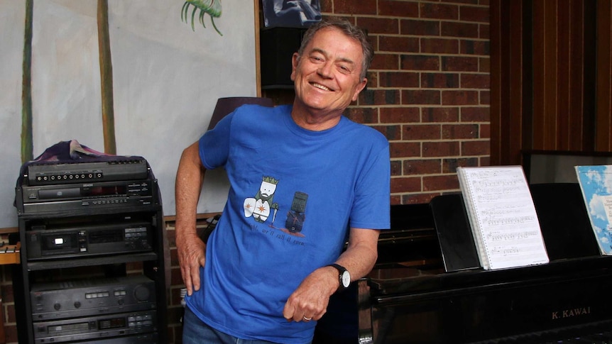 Children's entertainer Peter Combe leans against a piano.