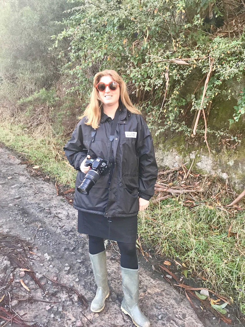 Georgina wearing gumboots standing on muddy, bush track while holding stills camera.