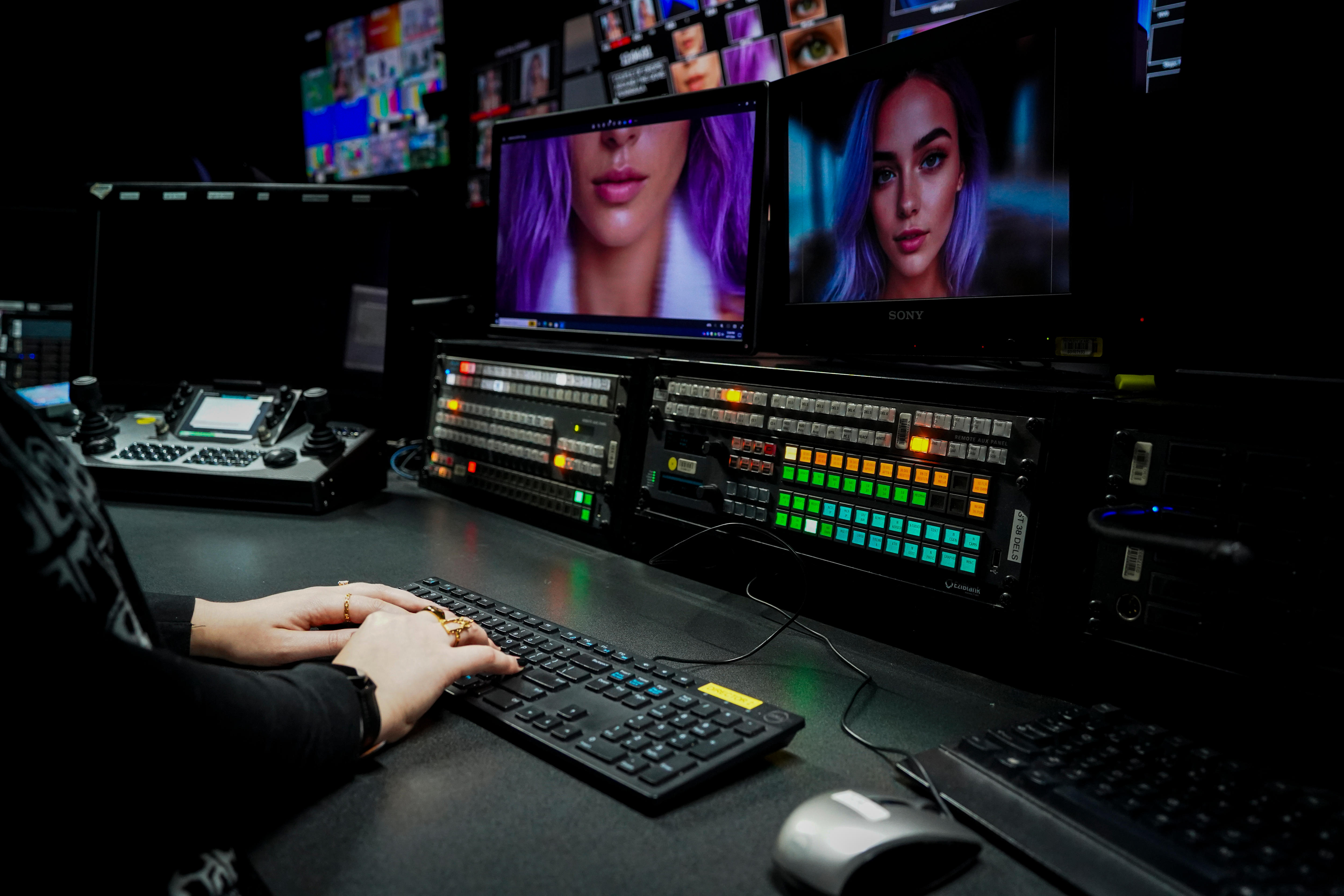 Fingers on a keyboard and multiple screens showing an AI woman.